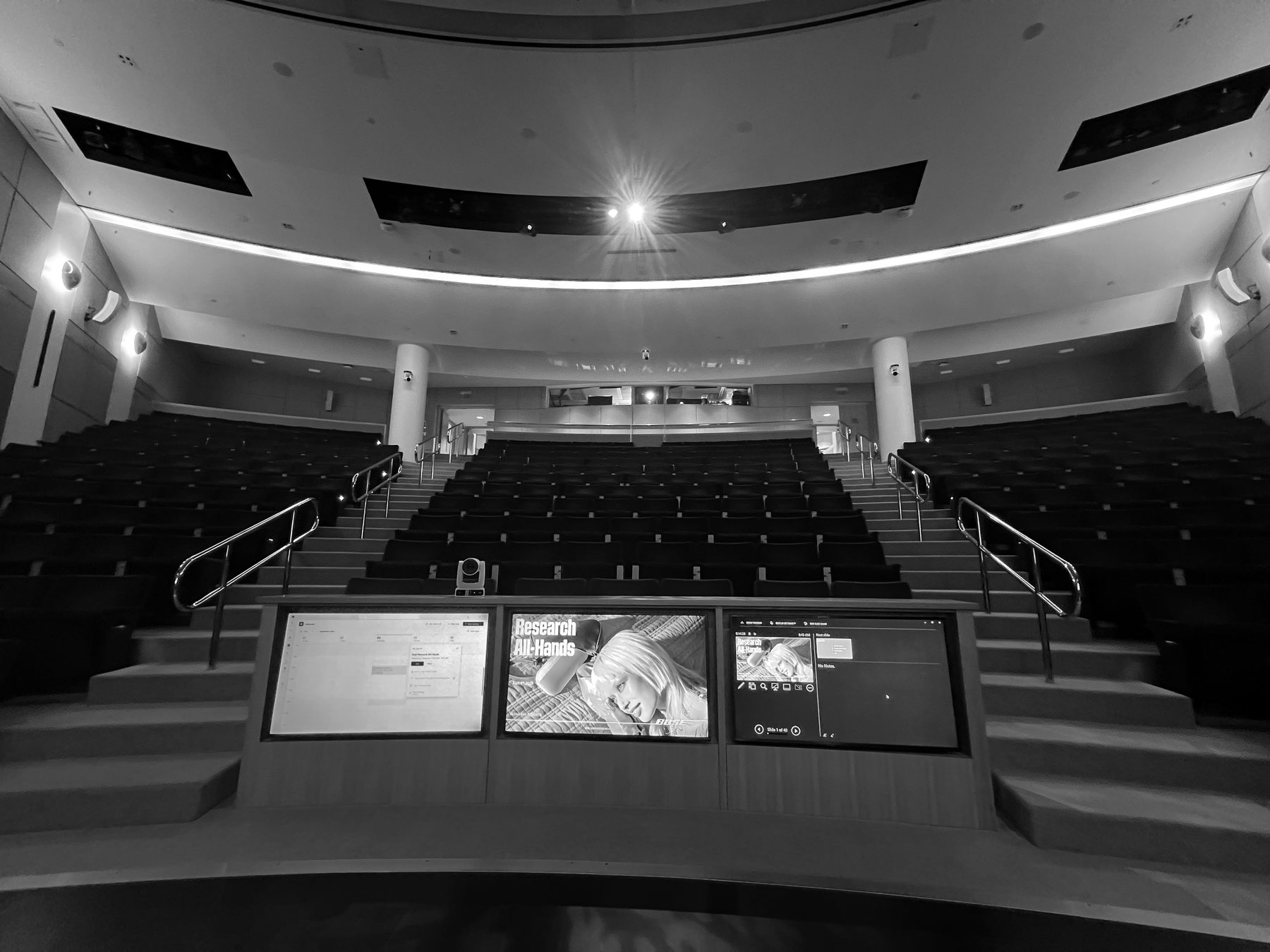 An empty auditorium with three screens lit on stage