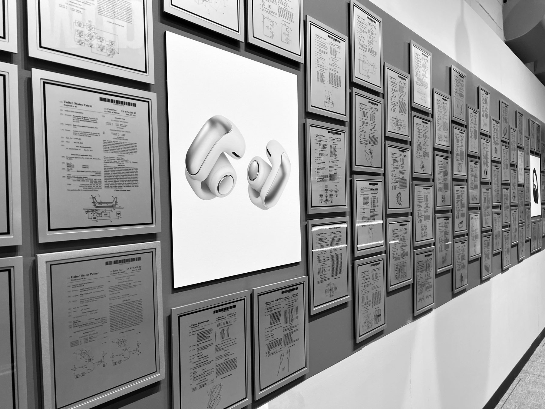 A wall of framed patents with a print of the Ultra Open Earbuds in the middle