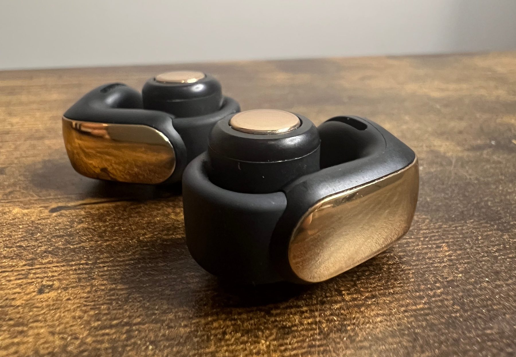 Bose Ultra Open Earbuds in black and brass on a wooden table
